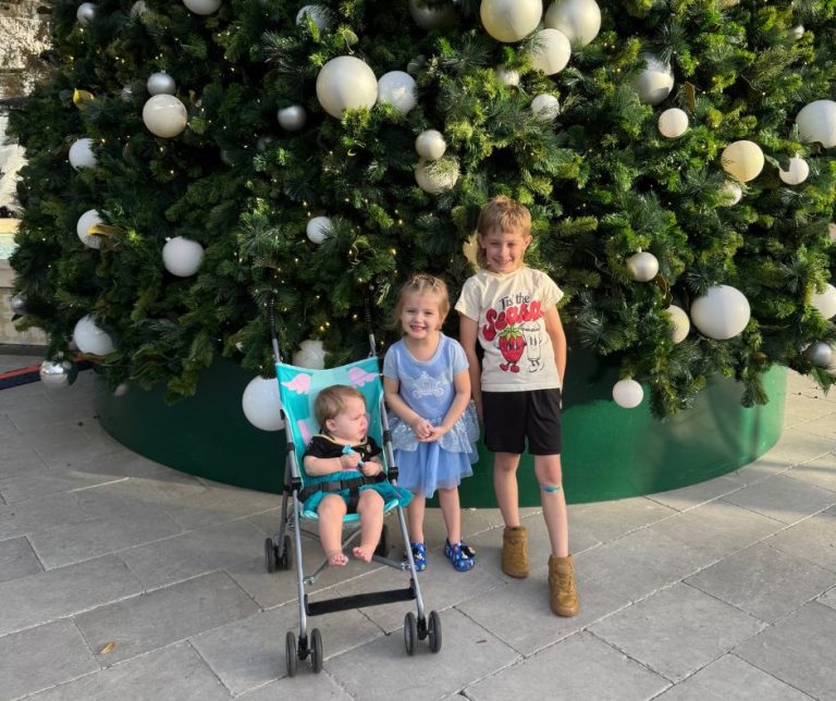 A picture of Sunni's 3 grandkids in front of a Christmas tree.
