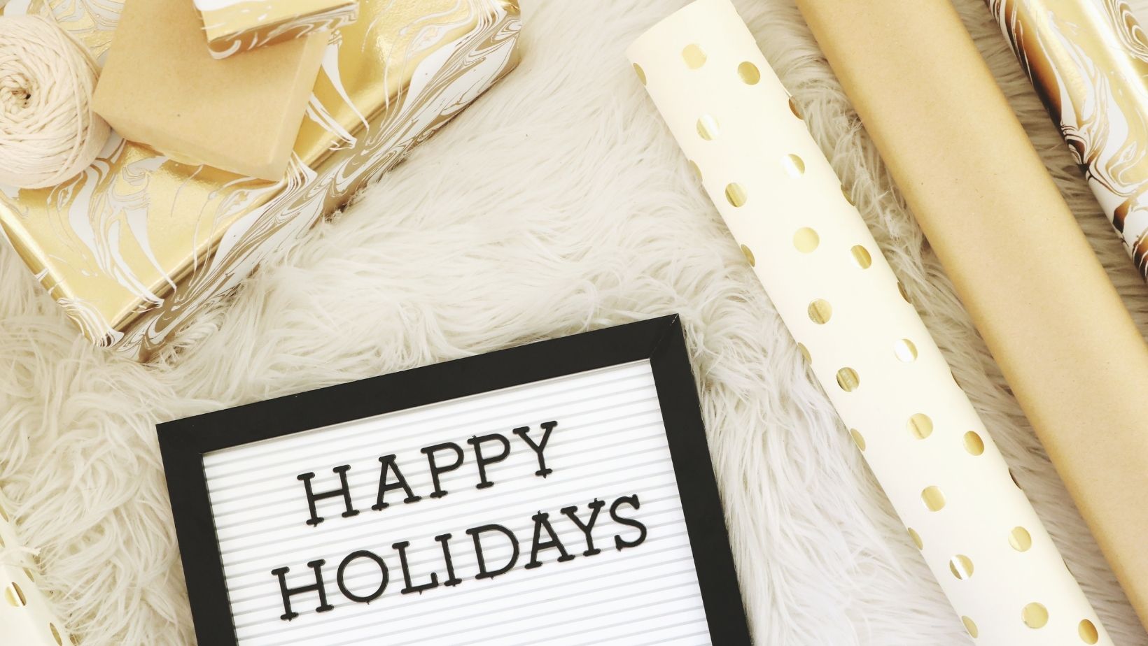 A Happy Holidays image of a fur blanket with wrapping paper, in gold and white tones.